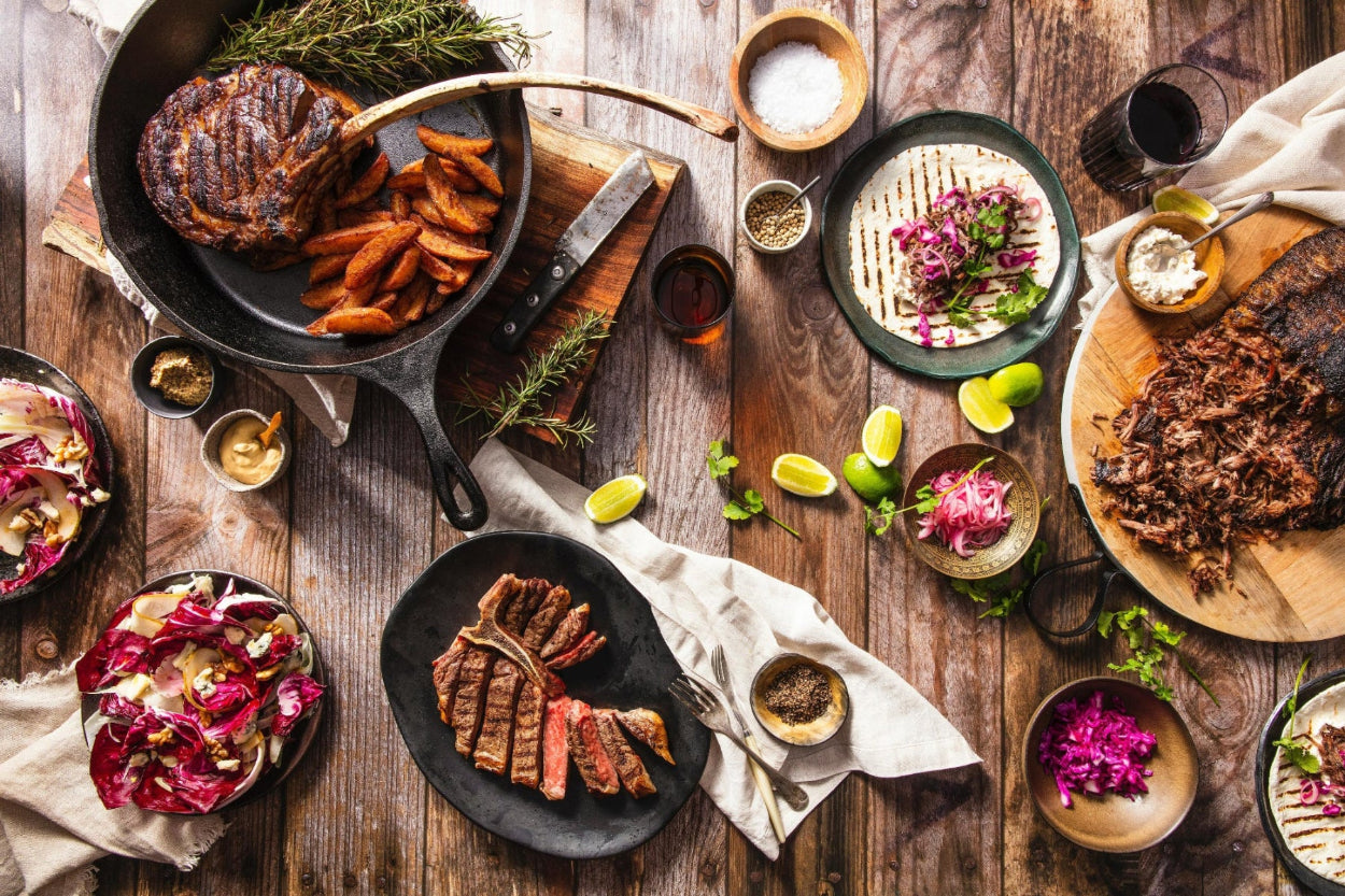 Assorted grilled meats and vegetables on a wooden table with various condiments.